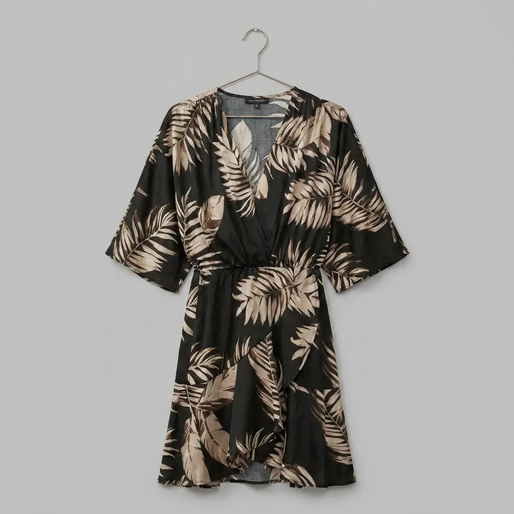 Mini wrap dress with batwing sleeves in black and gold palm leaf print on hanger