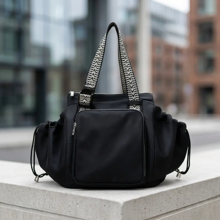 Black convertible tote with woven handles and silver zips on a concrete ledge