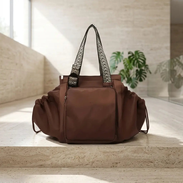 Brown convertible tote with ruched drawstring sides on a stone step
