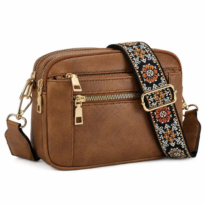Small structured crossbody camera bag in white with brown trim and zip closure, flat lay