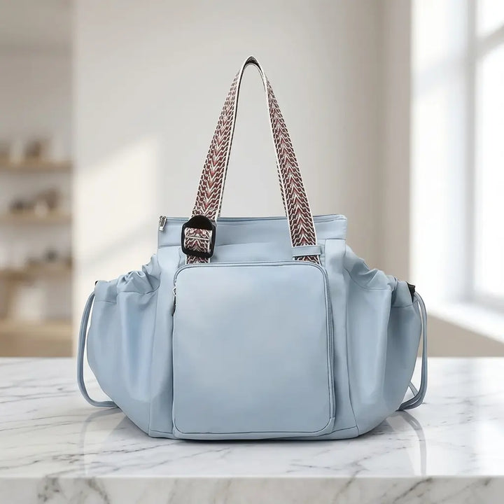 Light blue convertible tote with patterned woven handles on a marble surface