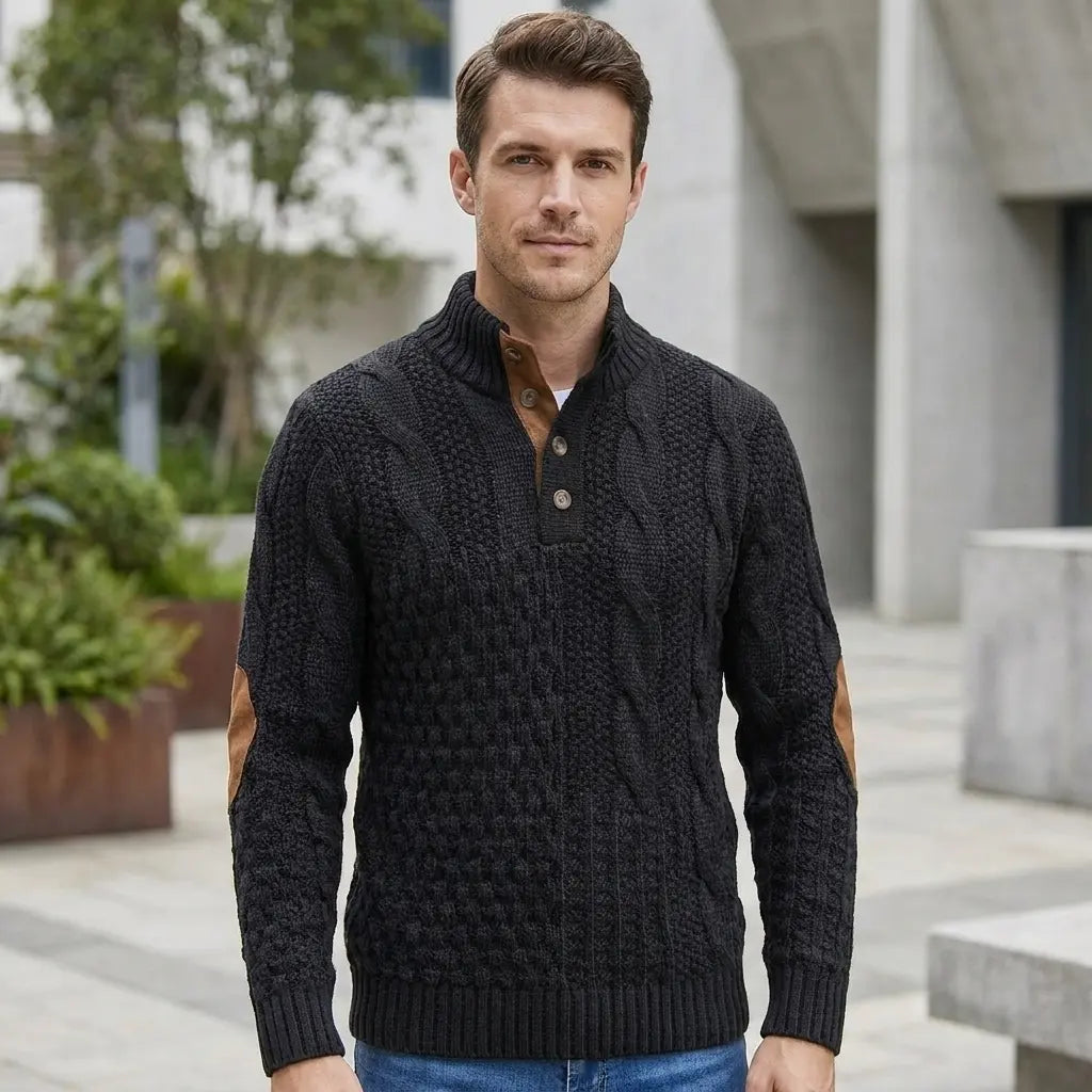 Men's cable knit sweater in black with elbow patches in outdoor setting, front model view