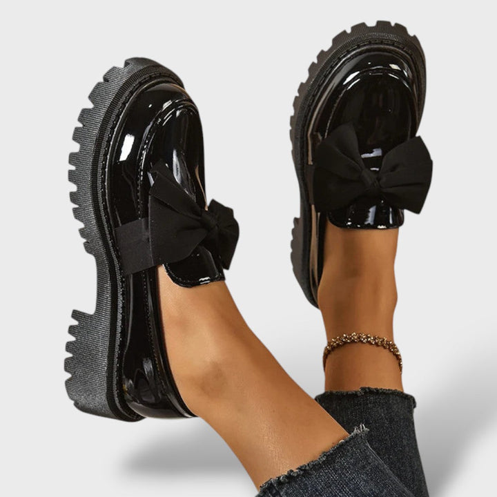 Black patent leather platform loafers with black bow, top and side view on raised feet