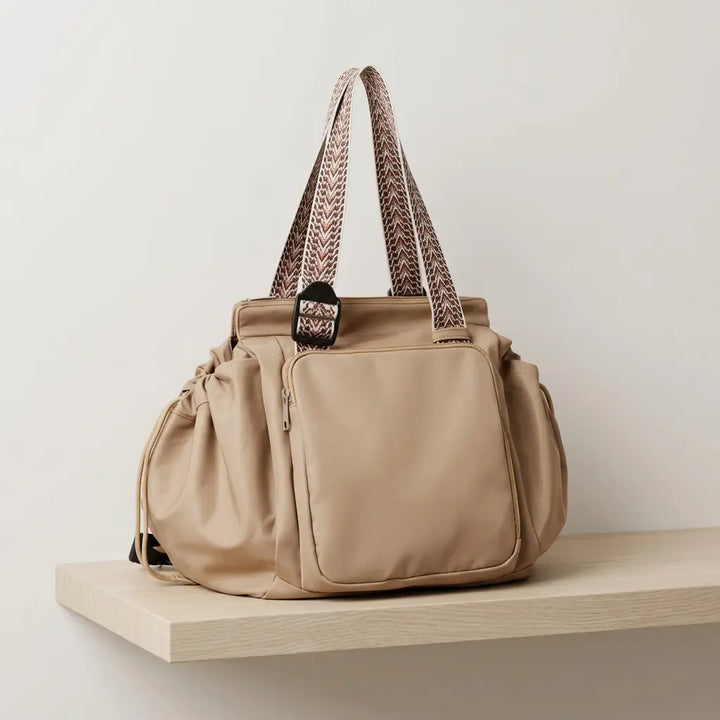 Sand beige convertible tote with woven handles resting on a wooden shelf