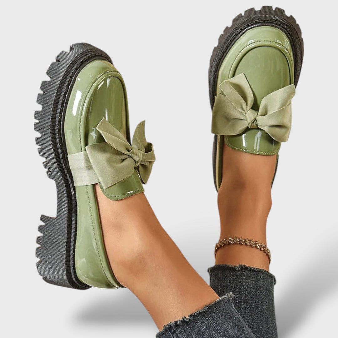 Sage green patent leather platform loafers with bow, sole and side view on raised feet