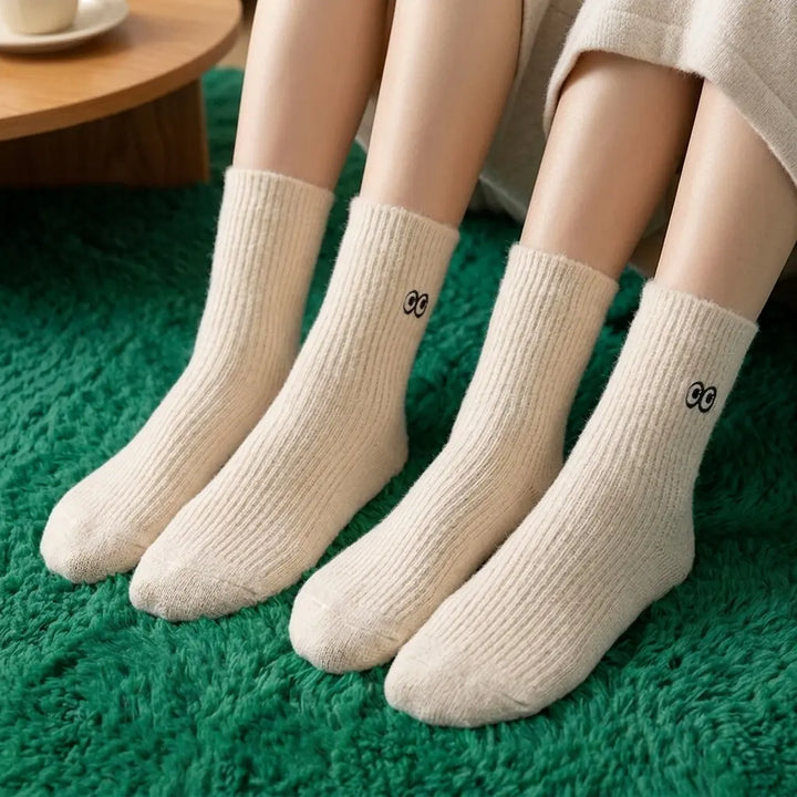 Two pairs of beige ribbed tube socks with embroidered cartoon eyes, close-up detail
