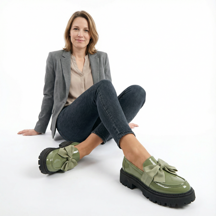 Sage green patent leather platform loafers with bow on seated model, styled with grey blazer and jeans
