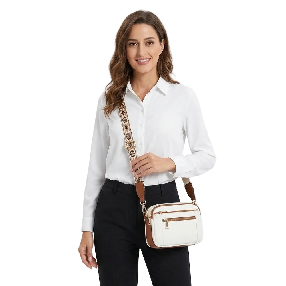 Model wearing small white crossbody camera bag with brown trim and patterned strap, front view
