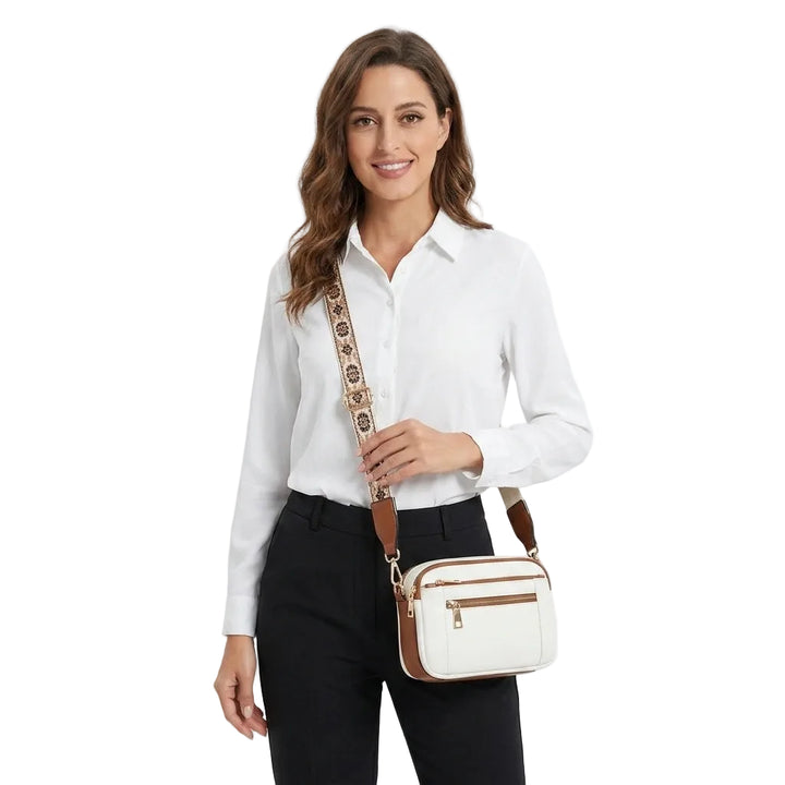 Model wearing small white crossbody camera bag with brown trim and patterned strap, front view