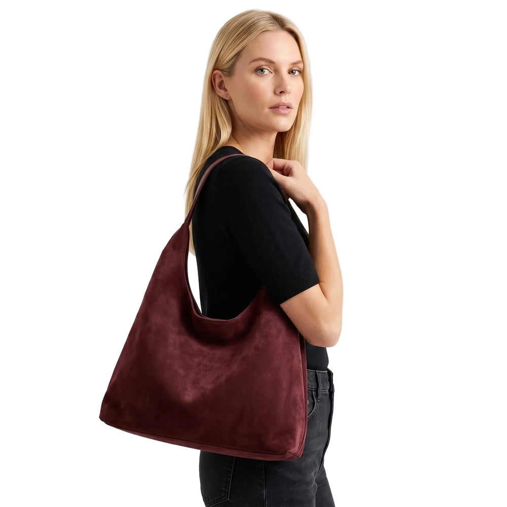 Woman carrying large slouchy hobo bag in deep burgundy suede, white studio