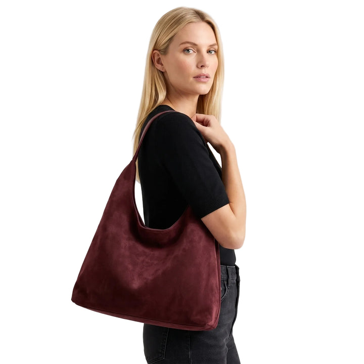 Woman carrying large slouchy hobo bag in deep burgundy suede, white studio
